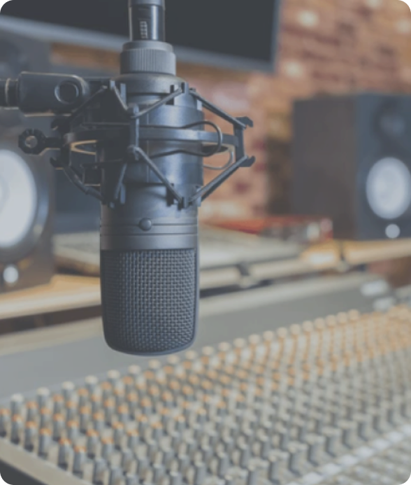 A high-quality studio microphone mounted on a shock mount, positioned in front of a large mixing console, with professional studio monitors in the background.