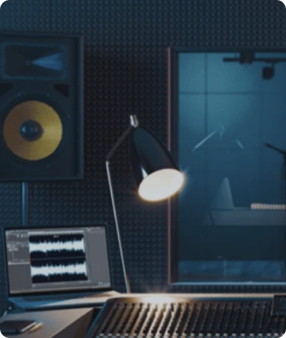 A professional recording studio with acoustic panels, a studio monitor speaker, a mixing console, and a soundproof recording booth visible through a window.
